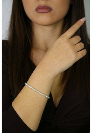 Bracciale d'argento con perle bianche piccole e distribuite uniformemente, indossato su un braccio nudo. La mano fa un gesto verso l'alto, mettendo in mostra il design del bracciale.