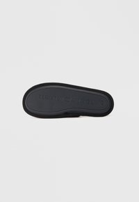 Suela de goma negra con patrón de agarre texturizado y marca en relieve. Bordes suaves, forma redondeada y diseño minimalista.