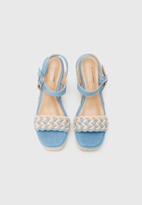 Blue denim sandals with a woven straw accent on the toe strap, adjustable ankle strap, and a low heel, featuring a smooth tan insole.
