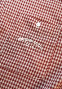 Κόκκινο και λευκό καρό ύφασμα με κουμπωτή τσέπη κεντημένη με το "HOUSE OF SUNNY" σε λευκό νήμα.