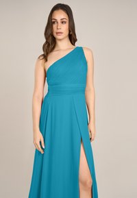 Türkises, einseitiges Kleid mit plissiertem Oberteil, tailliertem Bund und hohem Seitenschlitz, aus leichtem Stoff gefertigt. Glatte, fließende Textur.