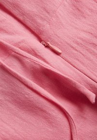 Tela de color rosa claro con una superficie texturizada, que presenta un cierre oculto y un detalle de superposición de tela, mejorando el diseño y la funcionalidad.