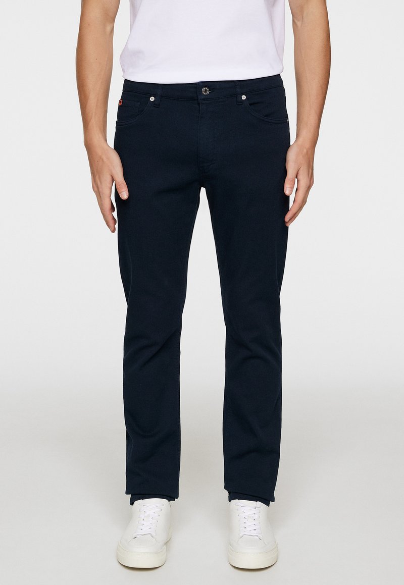 Tmavomodré bavlnené chinos nohavice so slim fit, dizajnom s piatimi vreckami, zapínaním na gombík a pútkami na opasok, skombinované s bielymi teniskami.