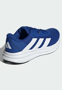 Modrá sportovní bota s síťovinovým svrškem, bílými akcenty, třemi bílými pruhy a silnou bílou podrážkou označenou jako "CLOUDCUSHION."