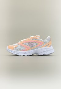 Αθλητικό παπούτσι σε ανοιχτό γκρι και ροδακινί χρώμα με λευκή σόλα, πάνελ από δίχτυ, και ροζ λογότυπο Lacoste στο πλάι, εμφανιζόμενο από την εξωτερική πλευρά.