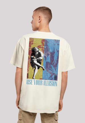 Cream cotton t-shirt with short sleeves, featuring a colorful graphic print on the back, text "USE YOUR ILLUSION," and a relaxed fit.