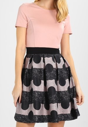 Vrouw die een roze top met korte mouwen draagt en een hoge taille rok met zwarte polka dots en horizontale strepen met een kanten patroon.