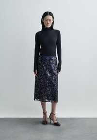 Μαύρο πουλόβερ με γιακά τύπου τέρμα σε συνδυασμό με μια διάφανη midi φούστα σε ναυτικό μπλε με λουλούδια. Η φούστα διαθέτει περίπλοκα σχέδια και εφαρμοστό λάστιχο στη μέση.