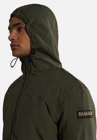 Giacca con cappuccio verde oliva dotata di chiusura con zip, cappuccio regolabile con cordino e una patch con il logo sulla spalla sinistra. Tessuto liscio.