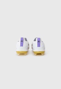 Scarpini da calcio bianchi con accenti viola, caratterizzati da un design testurizzato e sei tacchetti in plastica gialla sulla suola per garantire trazione.