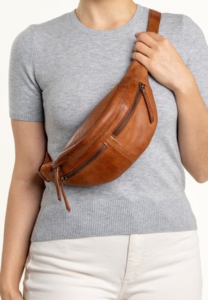 Marsupio in pelle marrone con due scomparti con cerniera, forma curva e una texture liscia. Indossato attraversato sul corpo. Top grigio chiaro visibile.