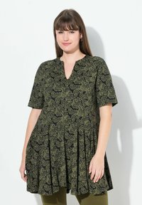 Vestido negro con mangas cortas, escote en V y falda plisada, que presenta un patrón de puntos verdes por toda la prenda. Textura de tejido suave.