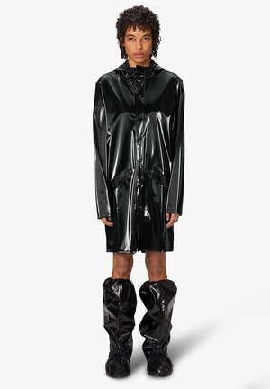 Chubasquero negro, brillante y largo, hecho de un material brillante, con capucha, bolsillos y combinado con botas de lluvia brillantes hasta la rodilla que hacen juego.
