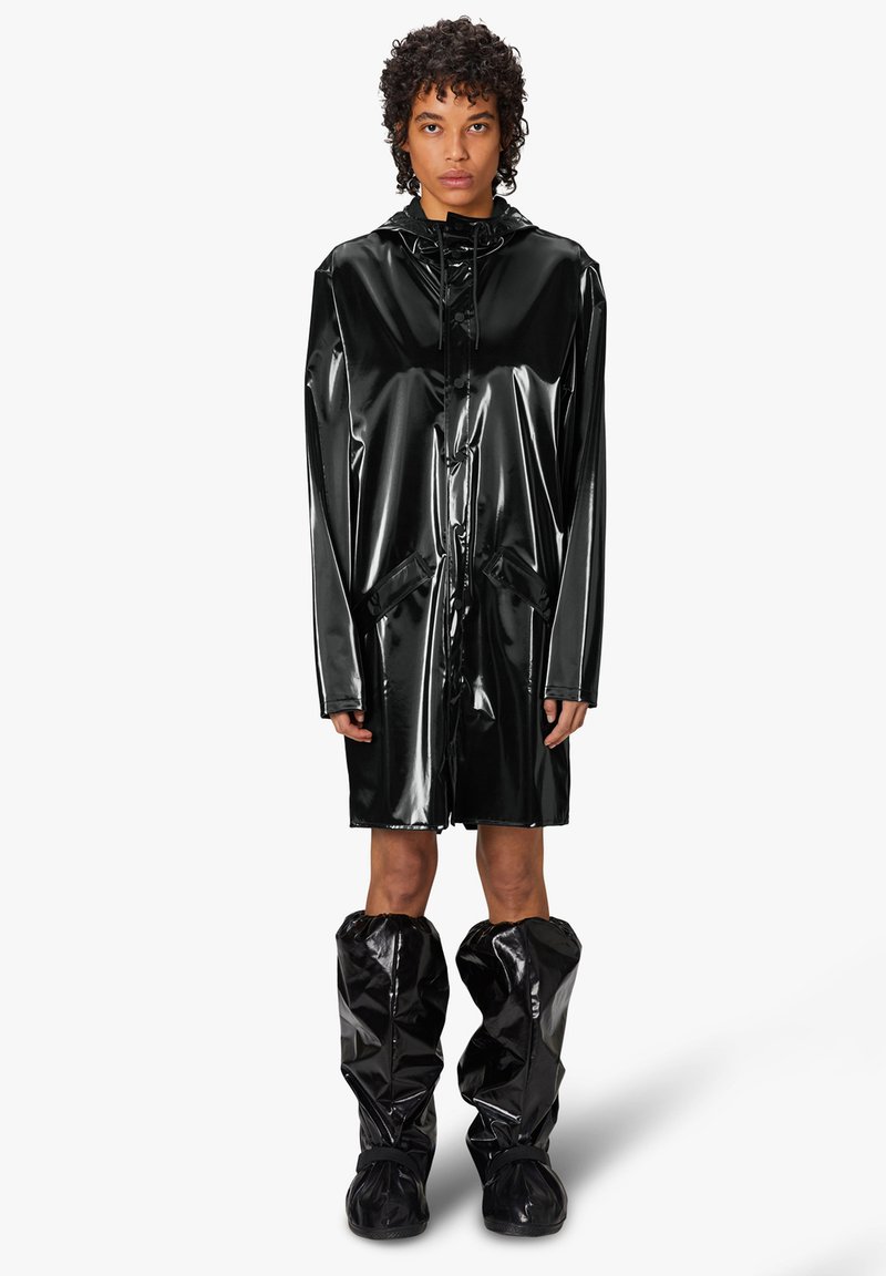 Chubasquero negro, brillante y largo, hecho de un material brillante, con capucha, bolsillos y combinado con botas de lluvia brillantes hasta la rodilla que hacen juego.