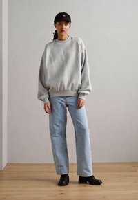 Sudadera oversized gris, jeans de pierna recta azul claro y botas negras. Textura ajustada de la sudadera, terminada con puños y dobladillo de canalé.