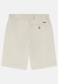 Pantaloni shorts color crema con vita elastica, dotati di una tasca posteriore con un bottone e di una piccola etichetta 'GUESS'. Tessuto in cotone morbido.