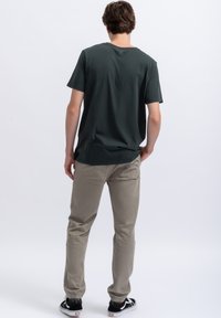 Donker groene t-shirt met een ronde hals, korte mouwen; gecombineerd met lichtgrijze broek; zwarte sneakers; eenvoudige uitstraling met minimale details.