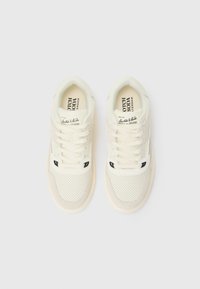 White sneakers with a perforated design, fabric and suede materials, flat laces, and a label on the tongue. Rounded toe and textured sole.