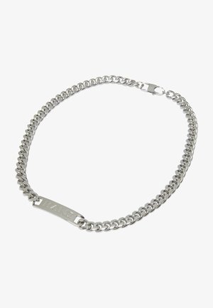 Stříbrný kovový náramek s proplétanými články a plochou obdélníkovou destičkou, na které je vyryto "KANI." Má bezpečné zapínání.