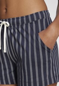Navy blue cotton shorts with white vertical stripes, featuring an elastic waistband with drawstring, side pockets, and a relaxed fit.