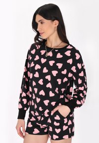 Svart topp med långa ärmar, tryckt med rosa hjärtan, kombinerad med matchande shorts. Båda plaggen är tillverkade av mjukt tyg och har en avslappnad passform.