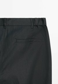 Black, textured fabric of pants with a flat waistband, hidden stitching, and a single rear pocket with a horizontal opening.