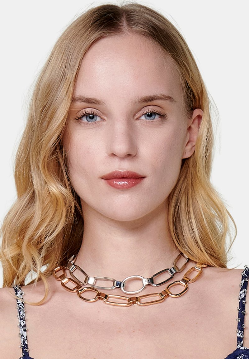 Collar de metal con eslabones alternos de plata y oro, que presenta una combinación de formas ovaladas y rectangulares. Acabado suave y brillante.