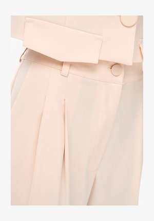 High-waist beige trousers with front pleats, matching fabric-covered buttons, belt loops, and a flap pocket detail.