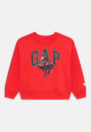 Sweatshirt vermelho com punhos e barra canelados, apresentando um grande logótipo "GAP". A imagem central mostra uma personagem em preto e vermelho.