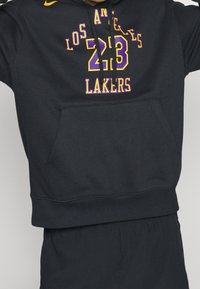 Hoodie noir ornée des inscriptions "Los Angeles Lakers" et "23" en texte violet et jaune. Comprend une poche frontale et une capuche avec cordon.
