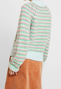 Suéter de punto con un diseño estampado en verde, rosa y blanco. Presenta un cuello y puños acanalados, con un ajuste oversized.
