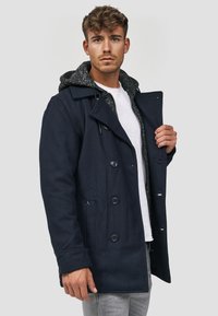 Marineblå ullblandingsfrakk med grå hette, dobbeltrykt knapplukking og sidelommer. Glatt tekstur, klassisk design.