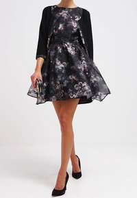 Svart klänning med blommönster, figurnära bodice och utsvängd kjol, lager på lager med en svart bolero. Matchad med svarta högklackade skor.