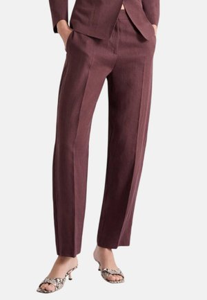Donna che indossa pantaloni eleganti color bordeaux a vita alta con gamba dritta e tasche laterali, abbinati a sandali con tacco aperti con stampa serpente.