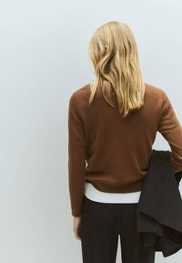 Brown crew-neck sweater made of soft material, worn over a white undershirt, paired with dark pinstripe trousers and a black blazer.