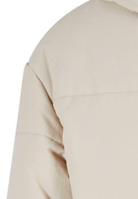 Beige pufferjacka med en slät textur, quiltad design och huva. Axelsömmarna har subtila sömnadsdetaljer.