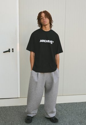 Sort oversized T-shirt med "ARCHIVE" logo i hvid, parret med grå sweatpants og sorte sko. Glat stof; afslappet pasform.
