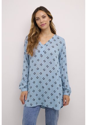 Blouse à manches longues bleu clair avec un col en V, ornée d'un motif floral noir, coupe ample et ourlet arrondi, fabriquée dans un tissu texturé.