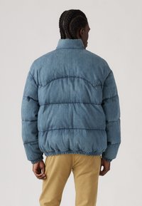 Lysblå dunjakke med quiltet design, elastisk nederdel og ærmer samt høj krave. Fremstillet af et struktureret, blødt materiale.