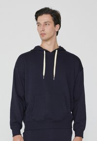 Marineblauer Hoodie aus weichem Stoff, mit einer vorderen Kängurutasche, beigen Kordeln und gerippten Bündchen und Saum.