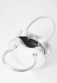 Stříbrná kovová kabelka s zaobleným designem, dvěma uchy, zipovým zapínáním a kontrastní tmavou podšívkou.