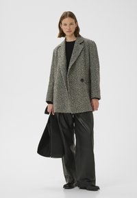 Grijze tweed oversized jas met notch revers, enkele knoopsluiting en twee voorzakken, gecombineerd met zwarte leren wijde broek.