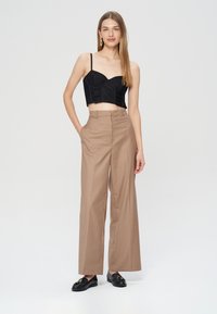 Czarny skórzany top z cienkimi ramiączkami, połączony z beżowymi szerokimi spodniami na wysokim stanie. Model ma na sobie czarne mokasyny i minimalistyczne kolczyki.