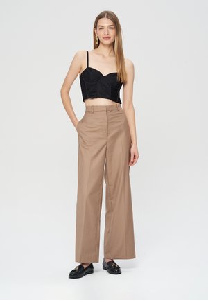 Czarny skórzany top z cienkimi ramiączkami, połączony z beżowymi szerokimi spodniami na wysokim stanie. Model ma na sobie czarne mokasyny i minimalistyczne kolczyki.