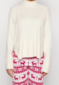 Maglione a collo alto di colore crema in morbido tessuto a maglia con dettagli a coste, abbinato a pantaloni da pigiama a righe rosse e bianche con motivi di renne.