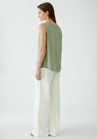 Haut sans manches, de couleur vert clair, avec un col rond, assorti à un large pantalon blanc. Texture lisse, coupe décontractée, fentes latérales discrètes.