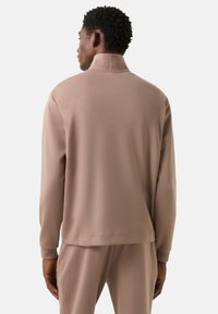 Světle hnědý pulovr s vysokým límcem, dlouhými rukávy a hladkou texturou. Jednoduchý design bez výrazných vzorů nebo zdobení.