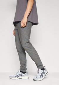 Pantalons à carreaux gris avec une coupe ajustée, fabriqués en tissu texturé. Associés à des baskets blanches et grises avec des accents noirs.