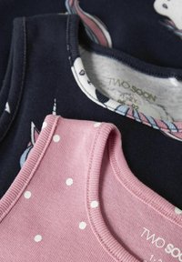 Deux débardeurs pour enfants : l'un rose avec des pois blancs, l'autre bleu marine foncé orné de graphiques de licornes. Matière en coton, encolures côtelées.