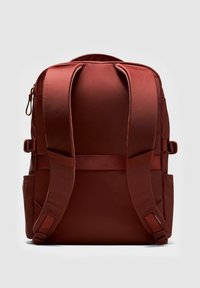 Sötét vörös hátizsák párnázott vállpántokkal, oldalzsebekkel és felső cipzárral, hátulról, egyszínű háttér előtt.